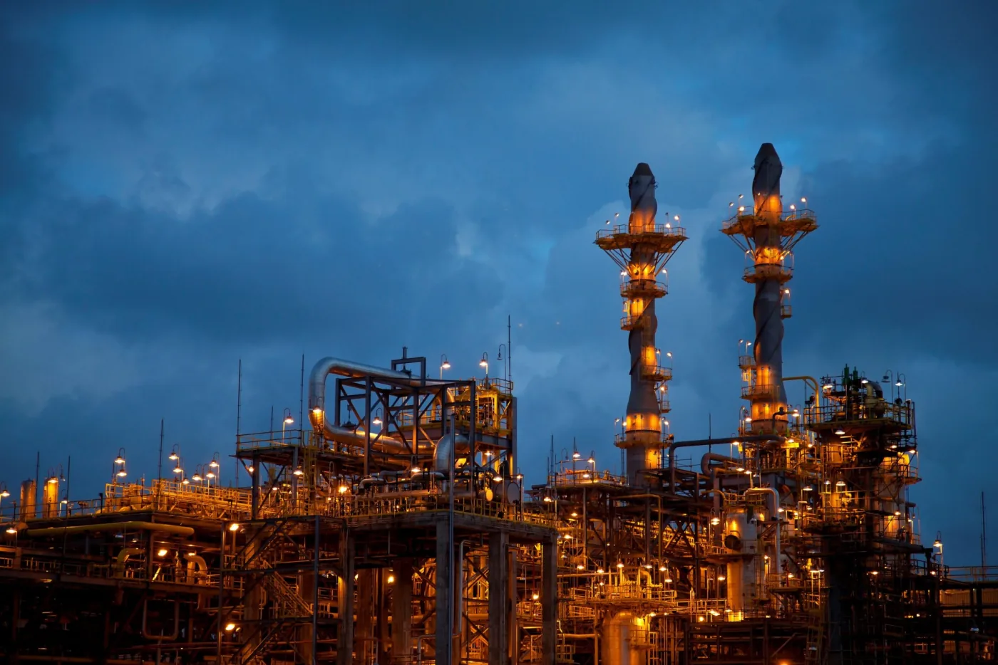 A refinery lit against a stormy evening sky.